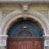 Ci avviciniamo al grande portone in legno, con lunettone ornato in ferro battuto, delimitato da due esili colonne corinzie con dadi brunelleschiani sui capitelli. Queste reggono un ampio archivolto dentellato, decorato con motivi vegetali nell�interno e con una testa felina in chiave